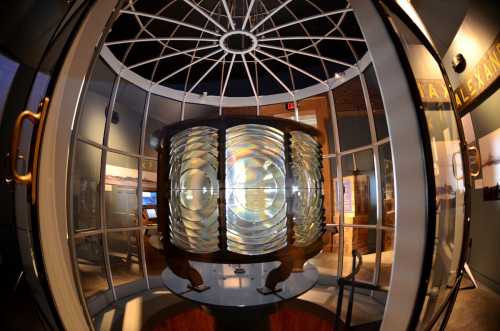 A large, circular glass display case containing a vintage lighthouse lens, illuminated from within.