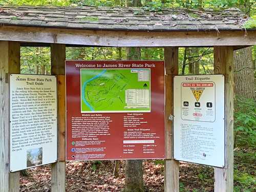 Sign at James River State Park displaying a trail guide, map, and trail etiquette information surrounded by trees.