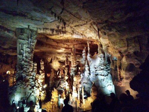 A dimly lit cave interior with stalactites and stalagmites, featuring visitors exploring the stunning rock formations.