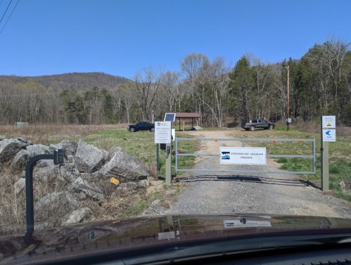A gated entrance to a nature reserve with a sign, surrounded by trees and a clear blue sky.
