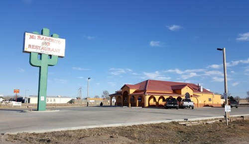 A colorful restaurant building with a cactus sign, set against a clear blue sky and open landscape.