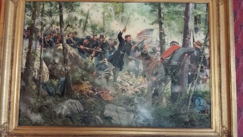A historical painting depicting a chaotic battle scene in a forest, with soldiers and an American flag amidst smoke.