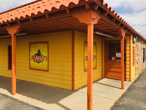 A colorful yellow building with orange trim and a tiled roof, featuring a sign that reads "Juanito's."