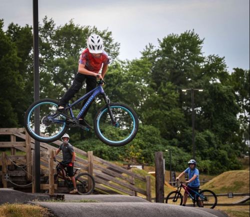A boy performs a jump on a BMX bike at a park, while two others watch nearby.