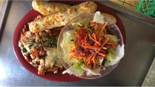 A red plate with cheesy pasta, two breadsticks, and a colorful salad in a bowl.