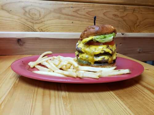 A towering cheeseburger with lettuce, tomato, and multiple cheese layers, served with a side of French fries on a red plate.