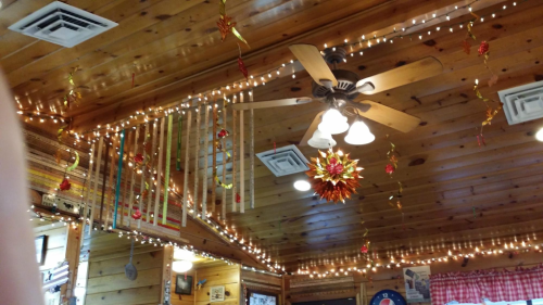 Cozy wooden interior with a ceiling fan, string lights, and festive decorations hanging from the beams.