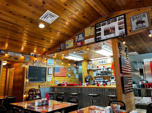 Cozy diner interior with wooden walls, vintage decor, an American flag, and a counter with stools and condiments.