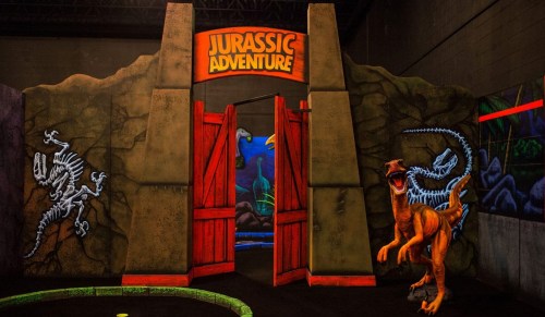 Entrance to a Jurassic Adventure attraction featuring dinosaur decorations and a vibrant, themed backdrop.