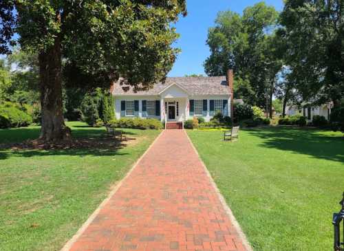 A charming house with a brick pathway, surrounded by green grass and trees on a sunny day.