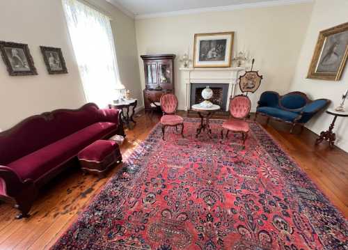 A vintage living room with a red rug, elegant furniture, and framed artwork on the walls.