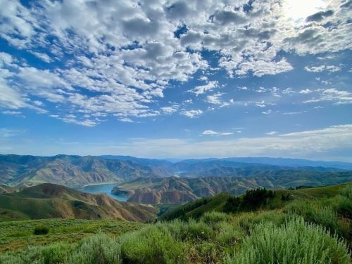 A panoramic view of rolling green hills and a serene lake under a partly cloudy sky.