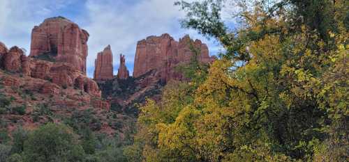 Scenic view of red rock formations and autumn foliage in a lush landscape under a cloudy sky.