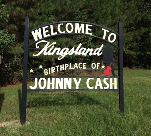 Sign welcoming visitors to Kingsland, birthplace of Johnny Cash, surrounded by greenery.