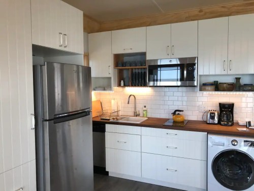 Modern kitchen with stainless steel appliances, white cabinets, and a wooden countertop. Bright and well-organized space.