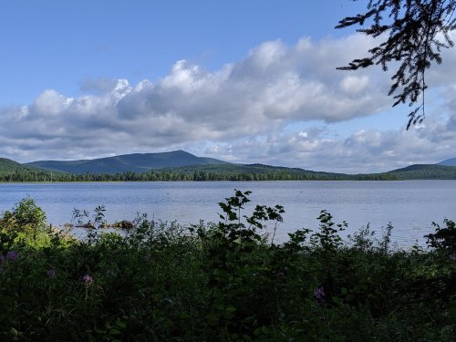 A serene lake surrounded by lush greenery and mountains under a partly cloudy sky.
