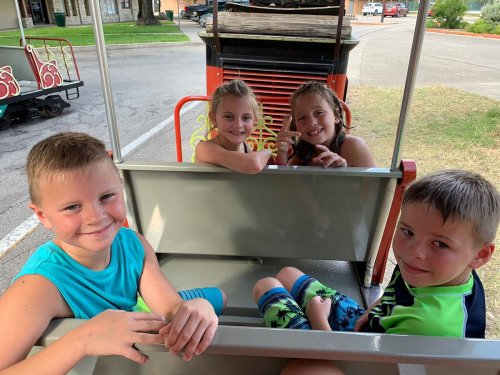 Four children sitting together in a cart, smiling and enjoying their time outdoors.