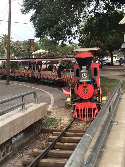 A colorful train with passengers on a track, surrounded by trees and a park setting.