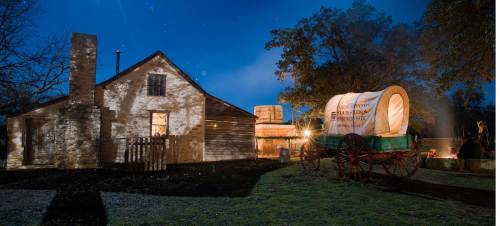 Historic building at night with a wagon, illuminated by soft lights and surrounded by trees.