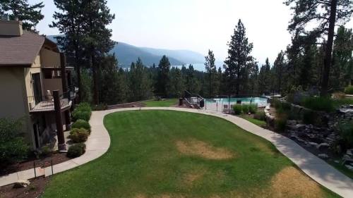 A scenic view of a landscaped yard with a pool, surrounded by trees and mountains in the background.