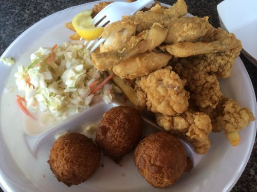 A plate of fried fish, coleslaw, fries, and two cornbread balls, garnished with a lemon wedge.