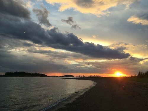 A serene beach at sunset, with clouds and a distant city skyline silhouetted against the colorful sky.