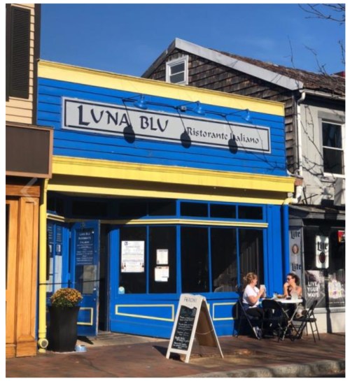 A bright blue restaurant with a yellow trim, "Luna Blu," featuring outdoor seating and two diners at a table.