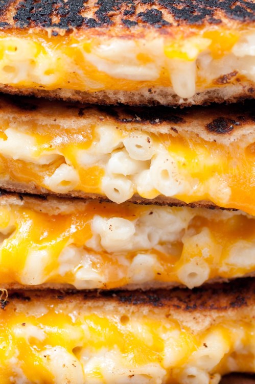 Close-up of stacked grilled cheese sandwiches filled with macaroni and cheese, showcasing melted cheese and crispy bread.