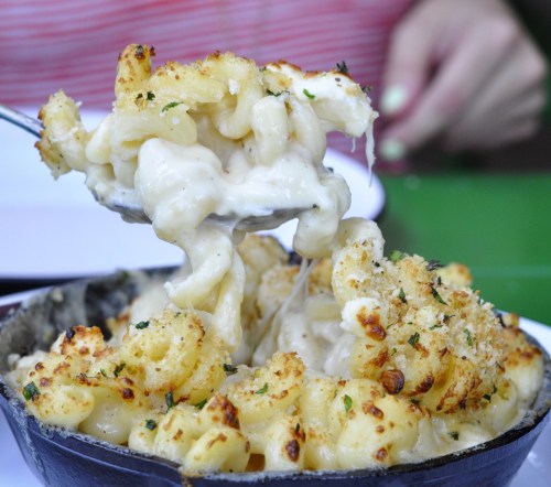 A close-up of creamy macaroni and cheese with a golden, crispy topping being served from a skillet.