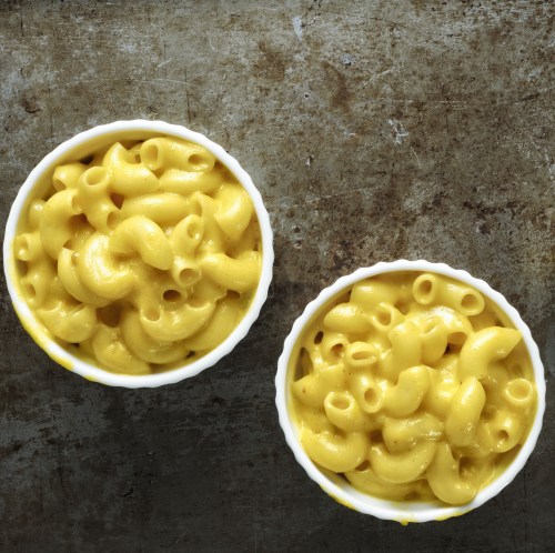 Two bowls of creamy macaroni and cheese on a textured metal surface.