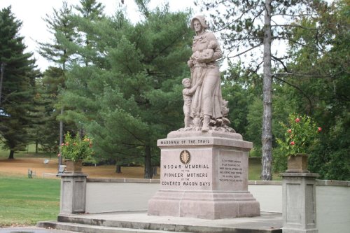 A stone monument depicting a woman with children, surrounded by trees and grass, honoring pioneer mothers.