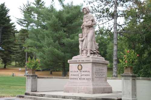 A stone monument depicting a woman with children, surrounded by trees and grass, honoring pioneer mothers.