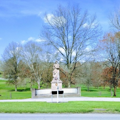 A statue on a pedestal surrounded by trees and a clear blue sky, set in a park-like area.