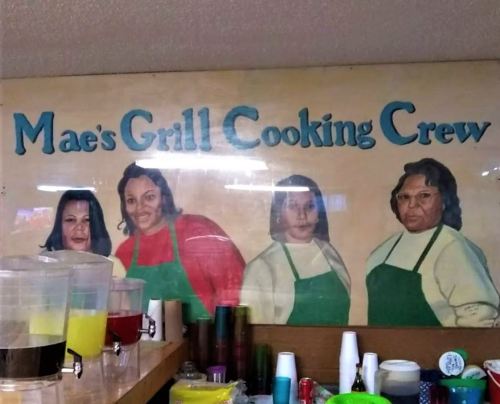 A mural of four women in green aprons, labeled "Mae's Grill Cooking Crew," displayed above kitchen supplies.