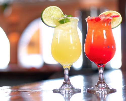 Two colorful cocktails in elegant glasses, one yellow with lime and mint, the other red with a lime slice.