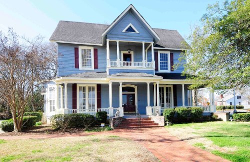 A large blue Victorian-style house with white trim, a front porch, and a well-maintained lawn.