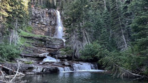 A serene waterfall cascades down rocky cliffs, surrounded by lush green trees and a tranquil pool below.