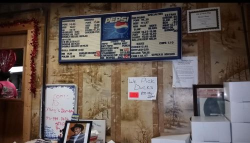 Menu board featuring food specials, Pepsi logo, and a sign that says "We Pick Ducks" in a rustic setting.