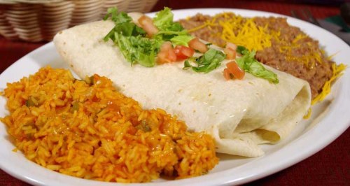 A plate featuring a burrito topped with lettuce and tomatoes, served with rice and refried beans.
