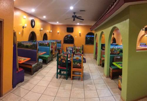 Colorful restaurant interior with vibrant tables and chairs, featuring a tiled floor and arched doorways.