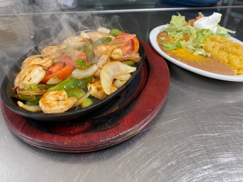 Sizzling shrimp fajitas with peppers and onions on a hot plate, served with rice and a side salad.