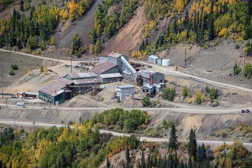 Aerial view of a mining facility surrounded by autumn-colored trees and rugged terrain.