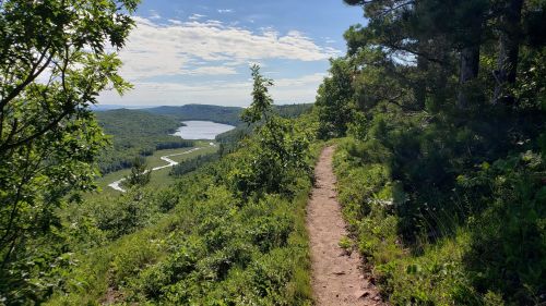 A scenic view from a hiking trail overlooking a winding river and lush green hills under a clear blue sky.