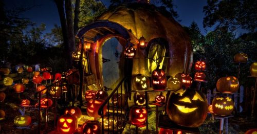 A whimsical pumpkin-shaped house surrounded by glowing jack-o'-lanterns in a nighttime Halloween setting.