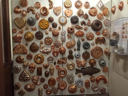 A wall display featuring an array of decorative copper molds in various shapes and sizes.