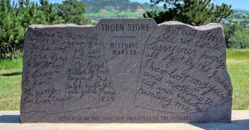 A stone historic marker with inscriptions about pioneers, set against a scenic landscape.