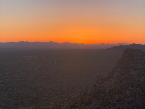 A serene sunset over a mountainous landscape, with vibrant orange hues illuminating the horizon.