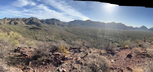 Panoramic view of a desert landscape with mountains in the distance and a bright sun shining above.