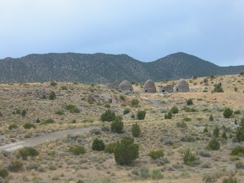 A landscape featuring stone structures on a grassy hillside, with mountains in the background under a cloudy sky.