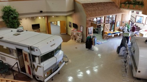 A spacious indoor area featuring two RVs, a merchandise display, and a cozy seating area with plants.